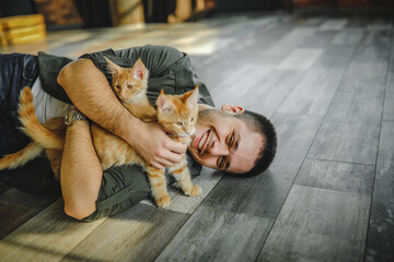 a young guy lies on the floor and hugs maine coon cats. Fun with kittens. Man in white T-shirt holding two kittens in hands. male cat lover. a man with a cat lying on his side