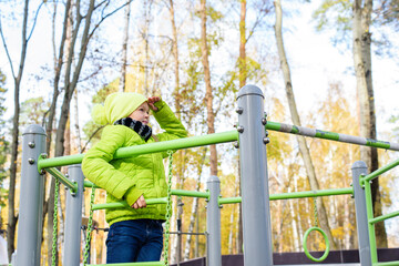 Beautiful teenager daughter in an green jacket plaing on the playground in the autumn park. Horizontal photo