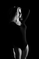 Young blonde plump woman with bright makeup in black bodysuit is posing at dark background, isolated with copy space. Concept of xxxl fashion and junk food