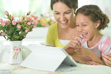 Happy mother and daughter using tablet together at home