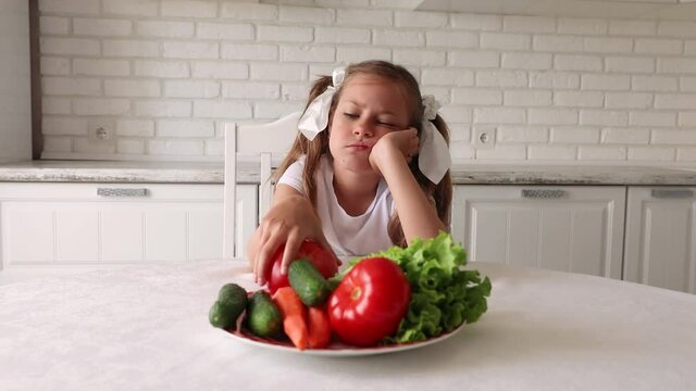 The little girl does not want to eat vegetables. Child gets angry and turns away. little girl in the kitchen does not want to eat healthy food