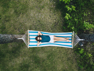 Girl resting in a hammock under tall trees, aerial view