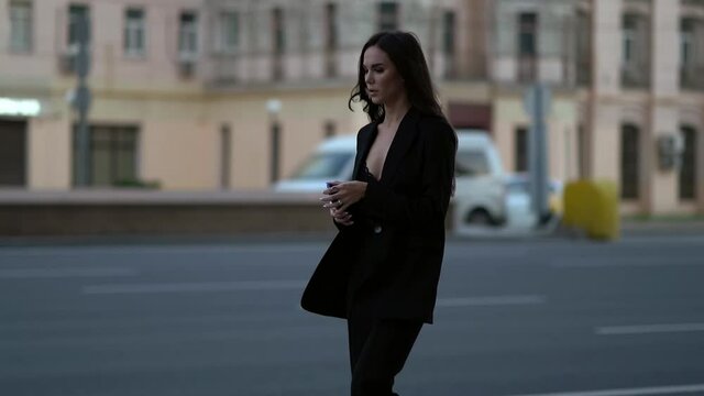 a young elegant slender woman walks along the road with a phone in her hand to a passing vehicle. Car lights on the background.