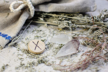 Scandinavian wooden rune Gebu, Gyfu on a rough linen cloth with amethyst crystalline, rock crystal and dried wormwood