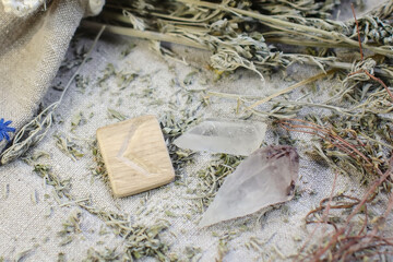 Scandinavian wooden rune Kauna, Kenaz on a rough linen cloth with amethyst crystalline, rock crystal and dried wormwood