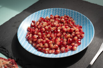 Pomegranate seeds on dish hard light over light green aqua menthe desk