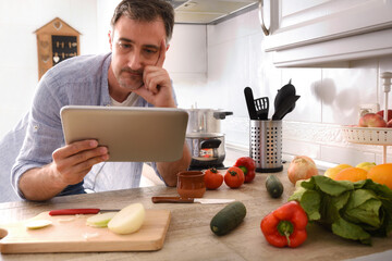 Doubtful man looking at recipe on a tablet at home