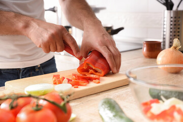 Hands cutting a pepper on cutting board on kitchen bench