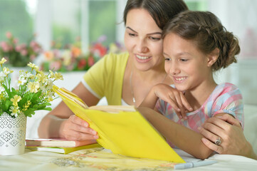 Cute girl reading book with mother at the table at home