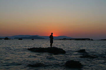 silhouette of a man fishing on the beach at sunset in Chania, Crete, Greece.