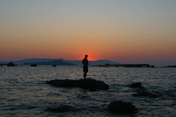 Fototapeta premium silhouette of a man fishing on the beach at sunset in Chania, Crete, Greece.