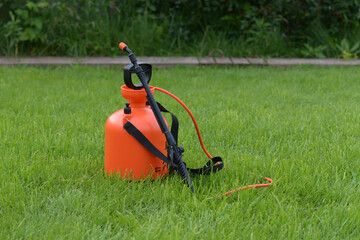 A garden water sprayer. Spray bottle. The orange sprayer is on a green lawn.