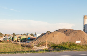 A large pile of sand at a cement factory against the backdrop of the sky, green grass, rural houses...