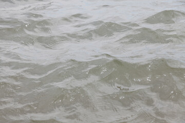 Close-up of a river with undulating waves with muddy gray water in cloudy weather. Background for wallpaper or screensaver on your desktop.