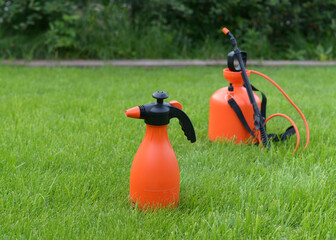 A garden water sprayer. Spray bottle. The orange sprayer is on a green lawn.