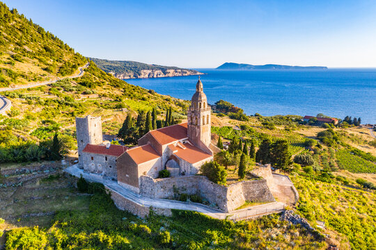 Aerial panoramic view of the cathedral St.Nicholas in Komiza city - the one of numerous port towns in Croatia, orange roofs of houses, picturisque bay, mountain is on background