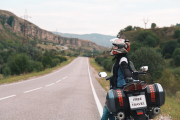 The woman in the helmet leaned against the bike. View of the road and mountain range