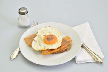 Sandwich with Bacon and fried Egg with Salt and Pepper on white Plate, closeup, isolated on white Background