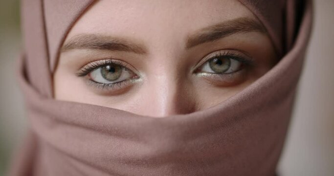 Face with natural make up of attractive muslim gir wearing traditional hijab scarf. Her brown and green eyes looking at camera - beauty, islam concept extreme close up 4k footage