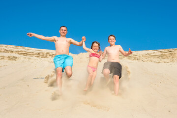 Family running on the beach sand on a sunny summer day. Family games on vacation. Sports and active lifestyle concept.