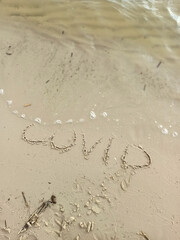 Word COVID written on the sand washes away with the wave 