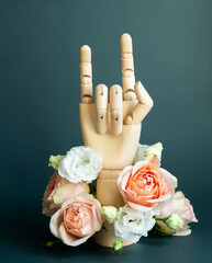 Wooden hand making Devil horns with flowers on dark green background. Creative concept with Rock n...