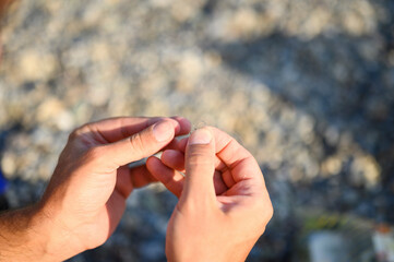 men's hands tying a fishing line on a fishing hook. selective focus. step 3
