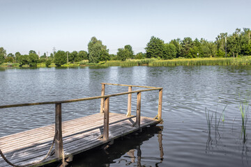 Fototapeta na wymiar Wooden pier on the lake. Rural landscape. Place of power. The beauty of the countryside. Pacification of nature. An ideal place for meditation. Boardwalk pier for fishing.