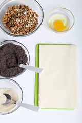 Ingredients for making puff pastry curls stuffed with poppy and walnut. Are laid out on a white table top.