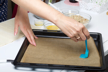 A woman lubricates parchment with sunflower oil. For making puff pastry curls with poppy and walnut...