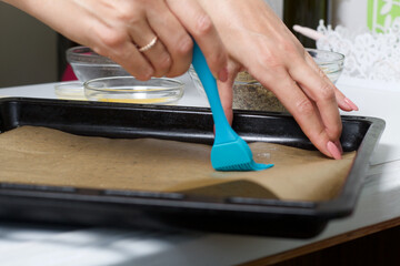 A woman lubricates parchment with sunflower oil. For making puff pastry curls with poppy and walnut filling.