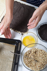 Woman sends poppy seeds puff pastry. For making puff pastry curls with poppy and walnut filling. Nearby on the table are ingredients and tools.