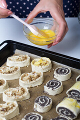 A woman smears an egg on curls stuffed with poppy and walnuts. For baking.