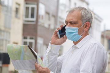 man in medical mask with a world map in his hand and in the other the mobile phone, concept of travel in the new normal