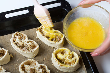 A woman smears an egg on curls stuffed with poppy and walnuts. For baking.