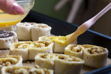 A woman smears an egg on curls stuffed with poppy and walnuts. For baking.