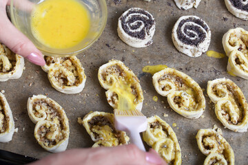 A woman smears an egg on curls stuffed with poppy and walnuts. For baking.