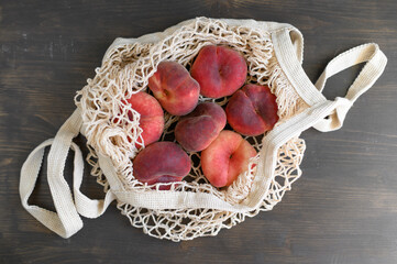 Ripe peaches in a string bag on a wooden background. Flat lay.
