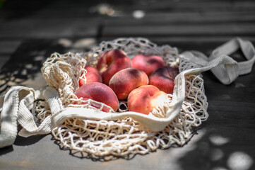 Ripe peaches in a string bag on a wooden background. Flat lay.