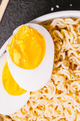 noodles in a plate with sesame seeds and soy sauce, bamboo sticks, boiled eggs on a black table close-up. flat ley. copy space.
