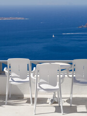 three white chairs with white table on the white terrace with blue sea view on a sunny day, without people