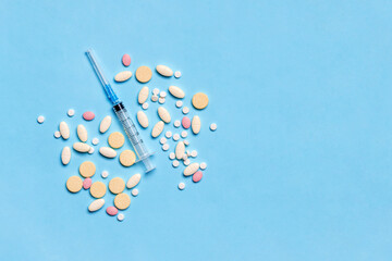 Medical syringe with tablets, pills on blue background with copy space. Injectable drugs,...