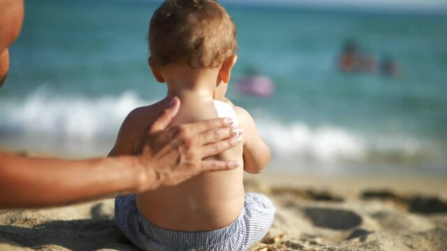 Close up of young mother hand is applying a protective sunscreen or sunblock lotion on her little toddler son back to take care of his delicate skin on a seaside beach during family holidays vacation.