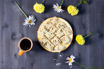 Obraz na płótnie Canvas Cookies with seeds on plate on black wooden table with yellow and white flowers, cup of coffee