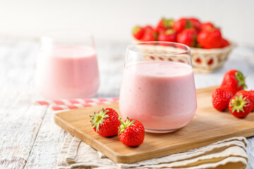 Glass with strawberry smoothie or milkshake on wooden table. Summer drink.