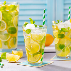 Lemonade, lemon, mint cocktail in glasses and jug. Blue background. Close up.