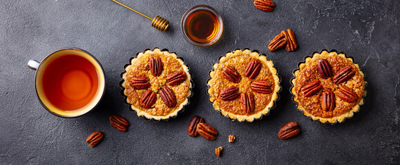 Pecan pies, mini tarts with cup of tea. Dark background. Close up. Top view.