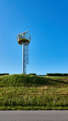 White measuring tower with yellow railings on a small hill, in front of it green meadow. Zeeland,...