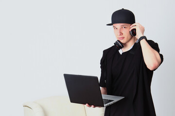 A young man in a black tracksuit and cap is holding a laptop and headphones. The concept of distance learning. Online training during self-isolation. Home education. Copy of the space. Handsome man