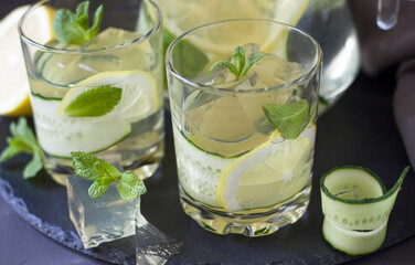 Two glasses of ice cold drink. ice cubes and mint leaves on a dark background. Lemon and cucumber...